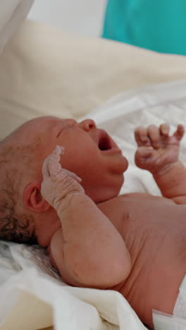 tiny newborn baby is being undressed by medics. child is unhappy and cries waving hands. close up. vertical video