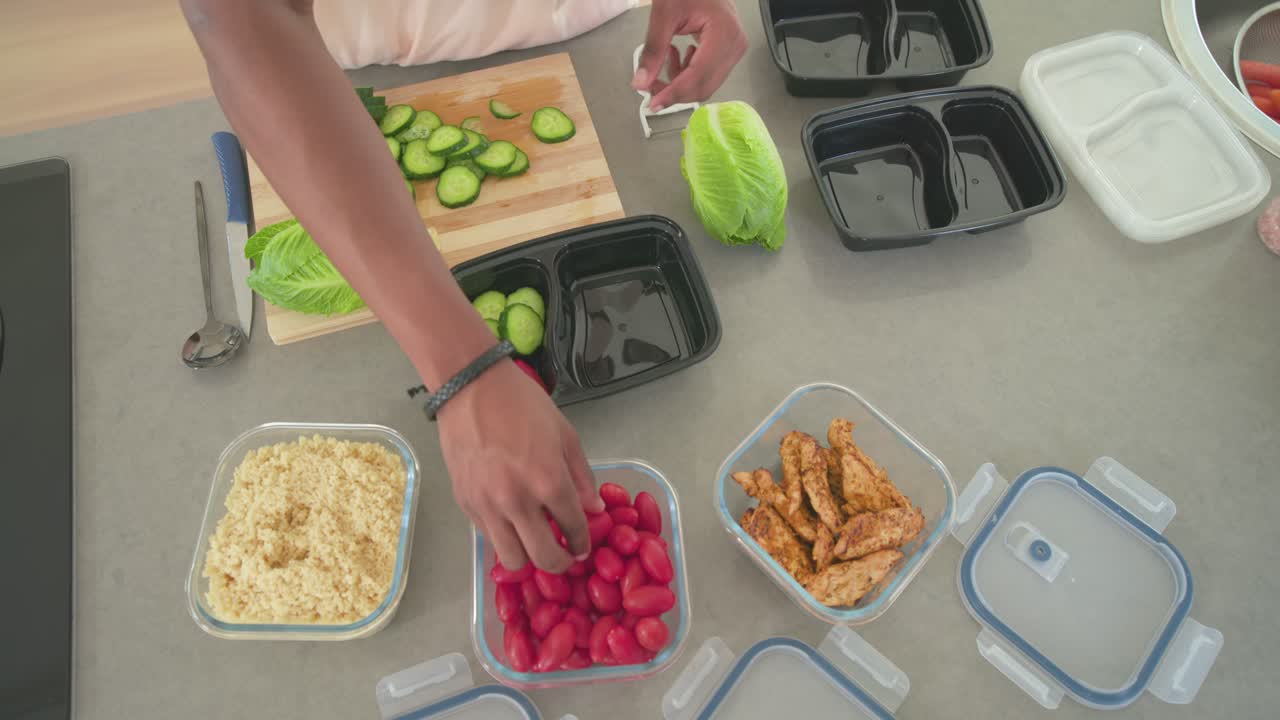African American man starting slicing cucumber, picking tomatoes, assembling meal boxes on counter