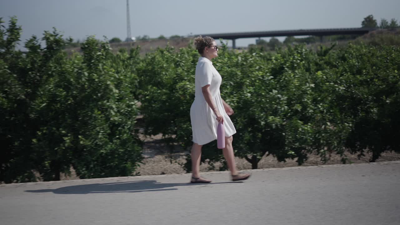 Woman Walking on a Road Lined with Trees