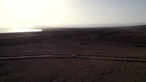 Aerial-view-of-cars-driving-the-desert-road,-sunset-weather-and-coastline