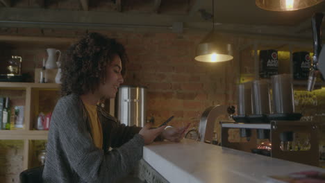 young woman is sitting in a cozy environment, checking the news on her phone and smiling