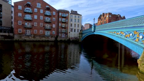 a bright, sunlit restaurant interior transitions to a scenic riverside view with a blue ornamental bridge and historic brick buildings in leeds, england
