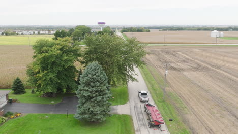 pickup truck transporting combine harvester header on rural farm road, aerial