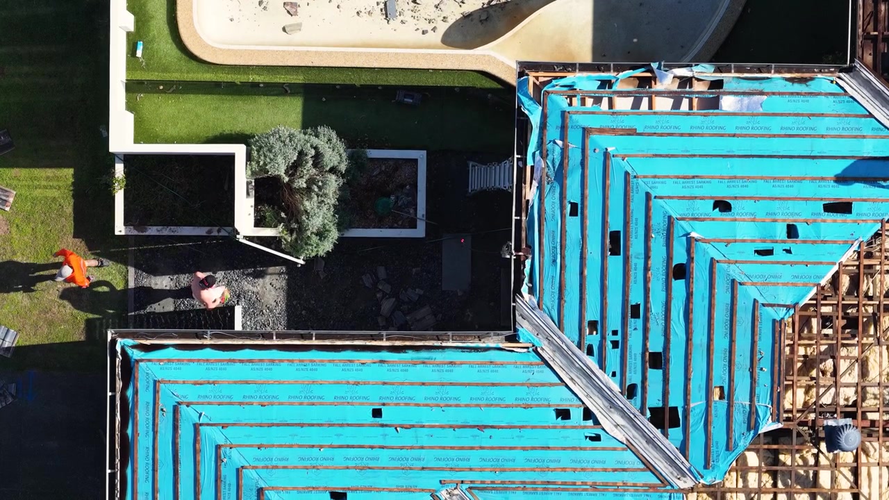 Aerial top-down drone shot of workers in orange shirts renovating a blue tarped roof.