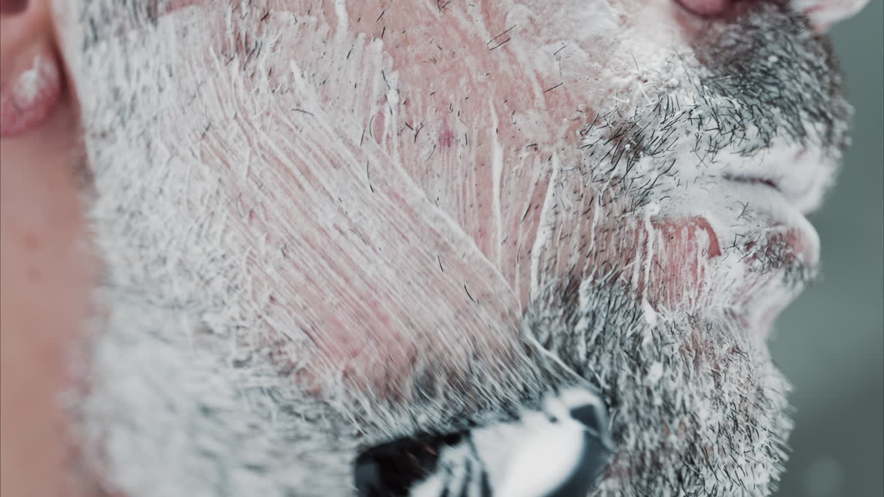 Close up of a man shaving his beard with a razor
