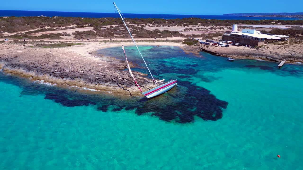 Sailboat stranded on cliff near the coast of Formentera Island, Spain, during a summer sunny day. Smooth aerial view flight descending drone
