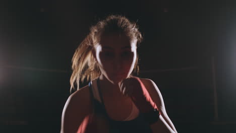 a beautiful female boxer strikes directly into the camera looking into the camera and moving forward on a dark background with a backlight. steadicam shot