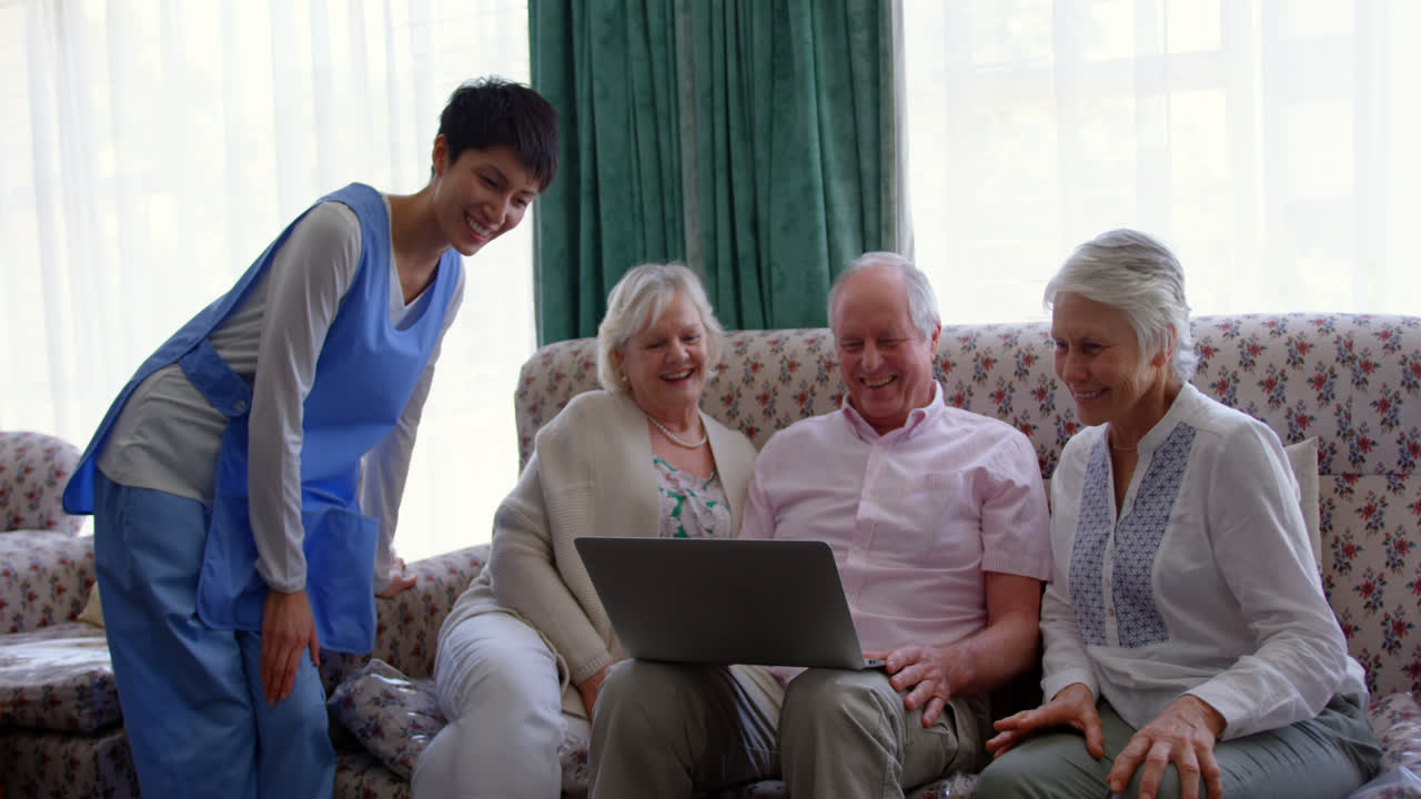 Vista frontal de amigos mayores caucásicos activos y una doctora usando un portátil en la residencia de ancianos 4k