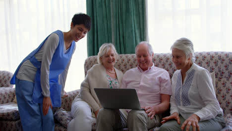 front view of active caucasian senior friends and female doctor using laptop in the nursing home 4k