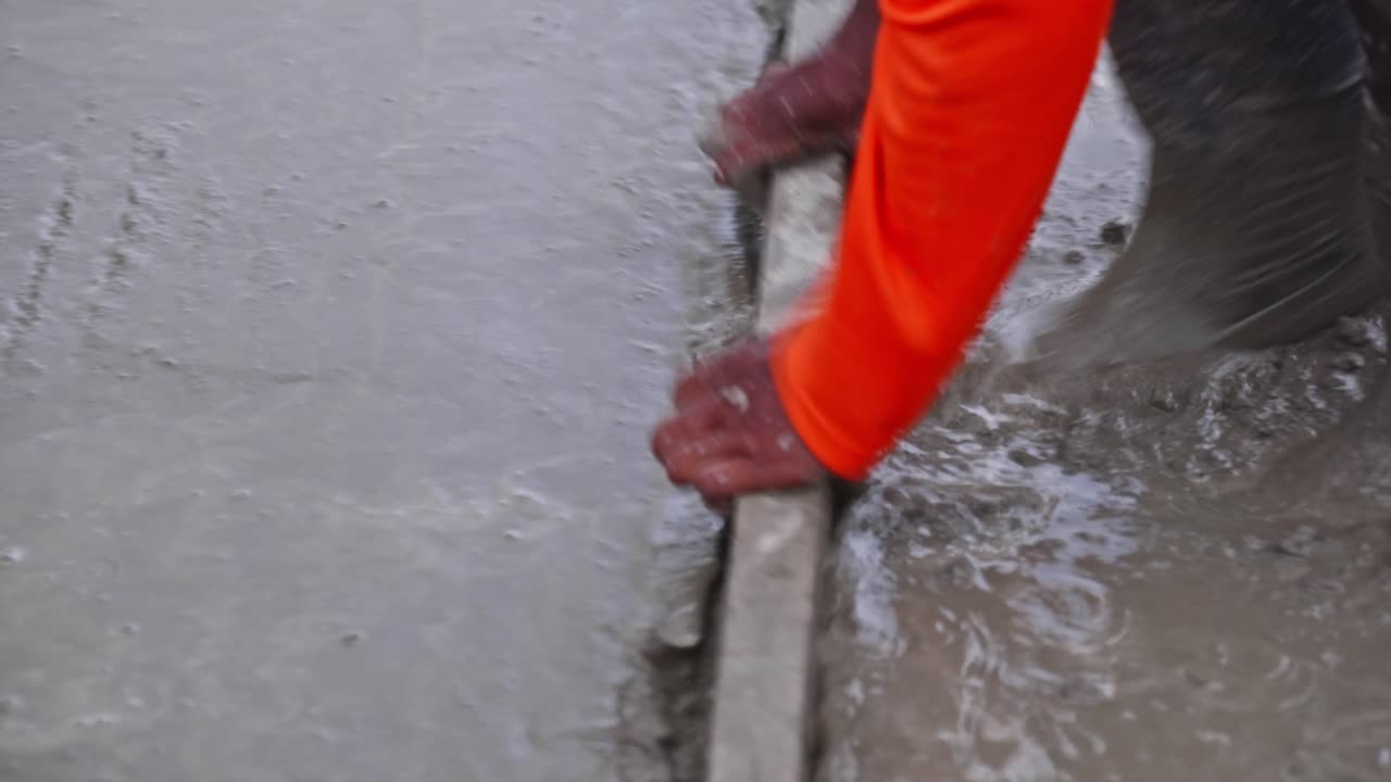 Worker Leveling Wet Concrete with straightedge tool on slab at construction site. day time, pan shot, 4k