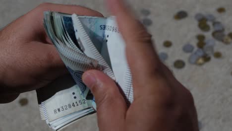 Man-hands-counting-Pakistan-currency-notes-of-1000-and-500-rupee-and-Pakistani-coins-in-the-background