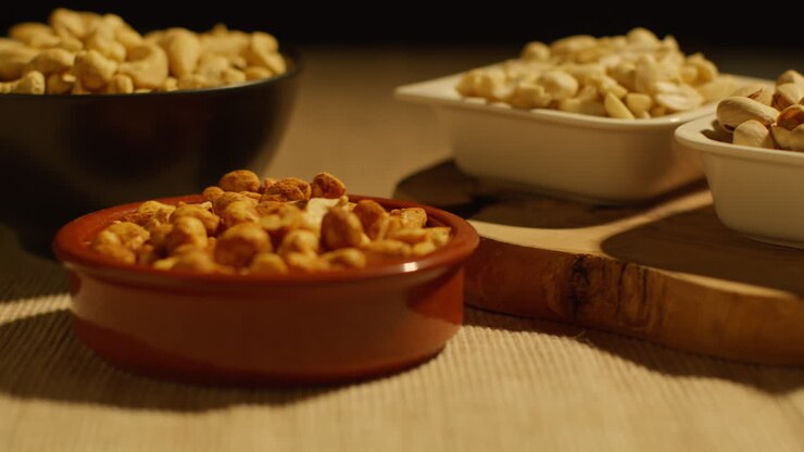 Close Up Of Hand Choosing From Bowls Of Cashews Dry Roasted Peanuts And Pistachio Nuts In Studio 1