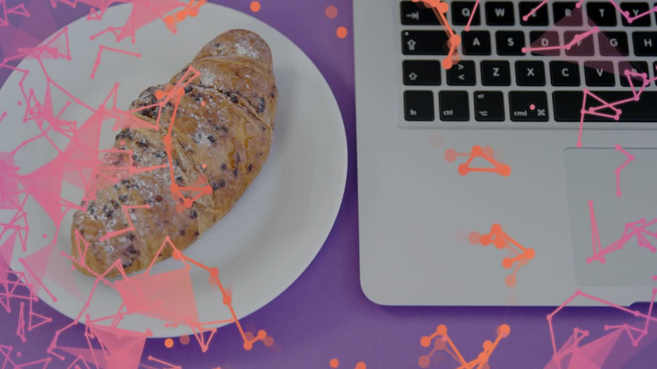 Triangular particles drifting, plate sliding, revealing croissant beside laptop for breakfast scene