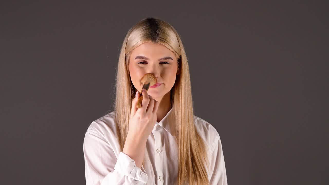 joven blanca feliz aplicando maquillaje, fondo de estudio marrón recortado