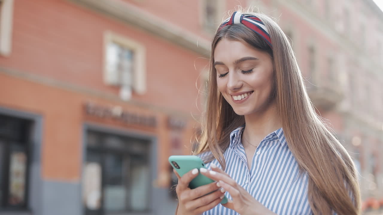 Mujer joven feliz sonriendo y usando su smartphone en la calle de la ciudad