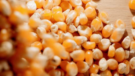 close-up spilling lots of dried corn kernels on a wooden table out of a brown paper bag until nearly all of the screen is covered