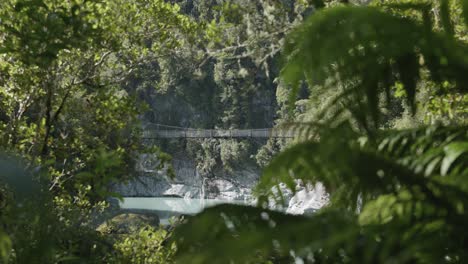 Detail-of-swingbridge-and-nature-over-Hokitika-river-flowing-through-Hokitika-Gorge-with-forests-on-a-sunny-summer-day-at-West-Coast,-New-Zealand