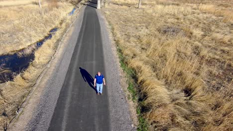 Senior-man-with-a-backpack-hiking-down-a-path-and-turning-onto-a-smaller-trail---aerial-orbit-view