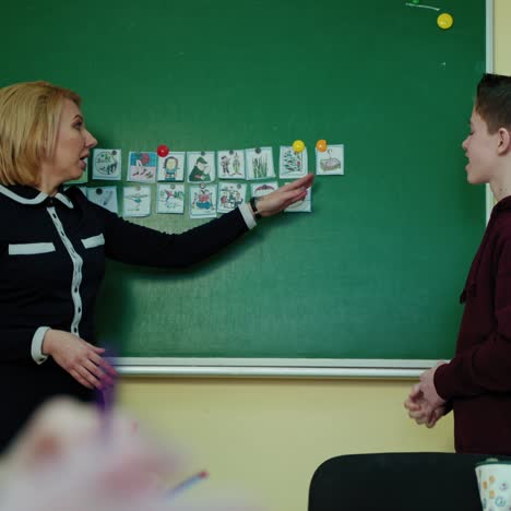 back to school. female teacher and a schoolboy near the blackboard. student speaks in the classroom while looking on pictures on chalkboard. education at school.