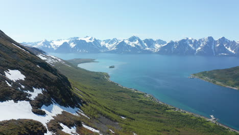 inclinación aérea hacia abajo, disparo de drone con vista a un pueblo y una carretera, en la costa del océano ártico, en un día soleado de verano, en rotsund, troms, nordland, noruega