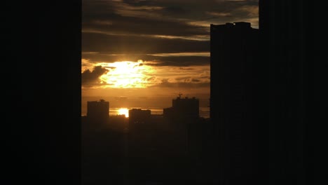 golden sun rising behind clouds with building silhouettes in foreground