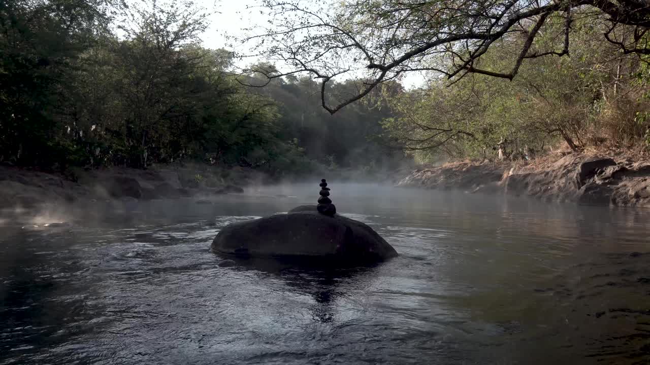 piedras oscuras equilibradas en los manantiales geotérmicos calientes de río caliente el salvador, tiro amplio de mano