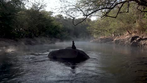 Balanced-dark-stones-on-the-hot-geothermal-springs-of-Rio-Caliente-El-Salvador,-Wide-handheld-shot