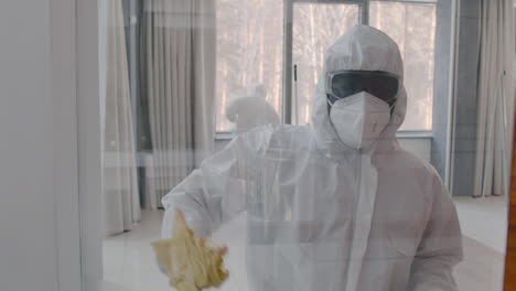 front view of a cleaning man wearing personal protective equipment cleaning window panes inside an office building