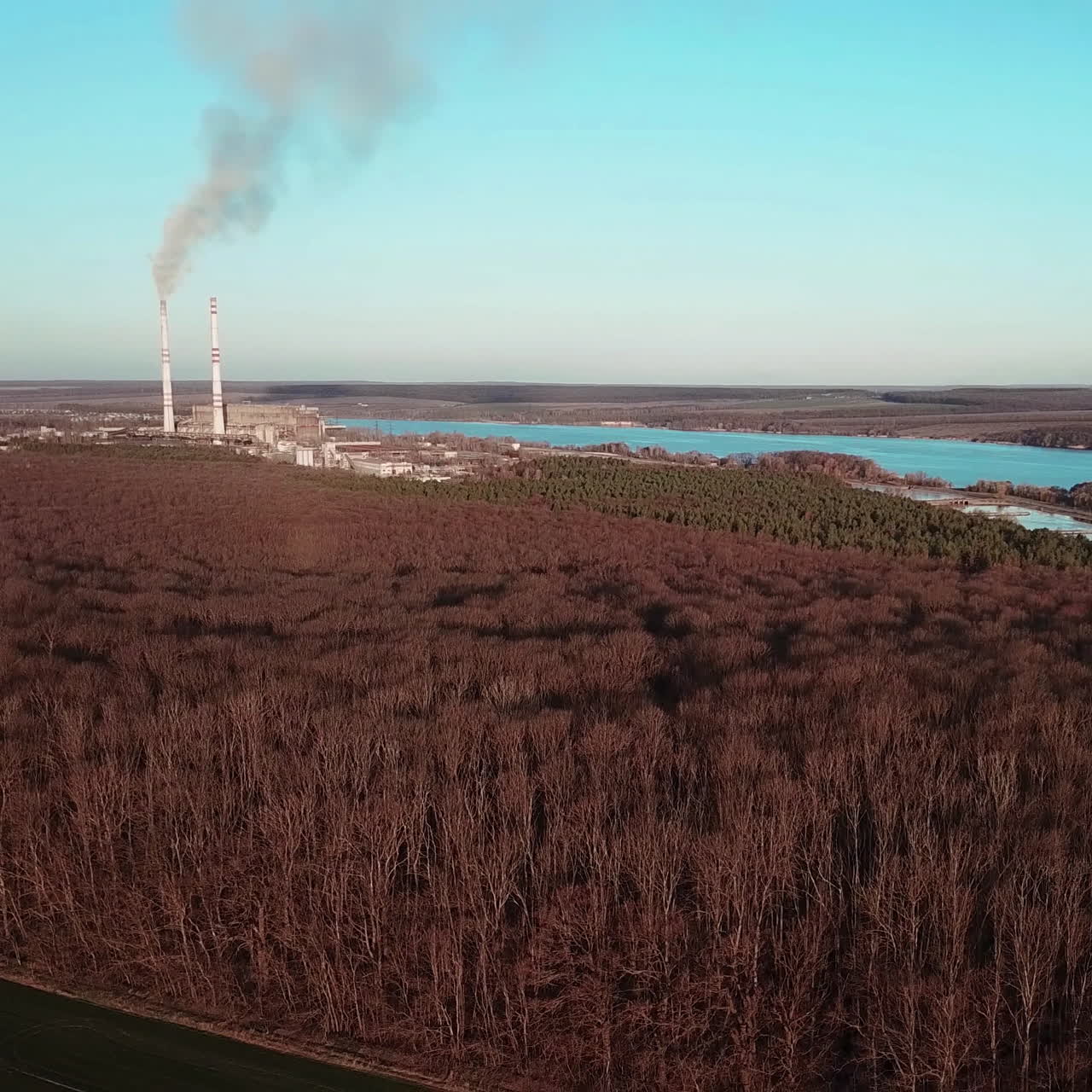 Aerial view of winter forest without snow against a background of a power station. Beautiful nature river