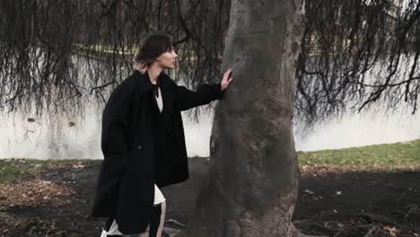 Mujer-Joven-En-Un-Abrigo-Negro-De-Pie-Bajo-Un-árbol-Ventoso-En-Un-Parque-En-Otoño-Por-La-Tarde-4