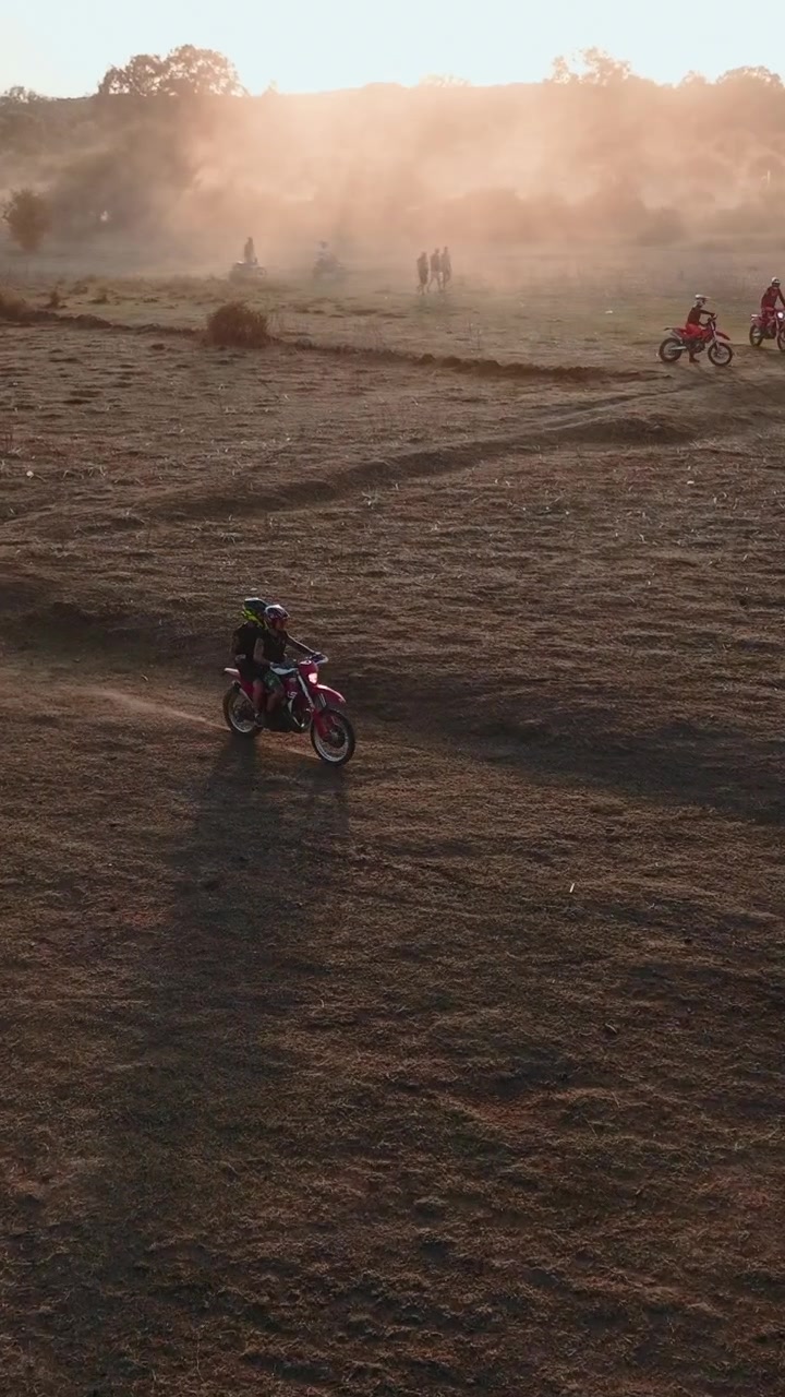 Motociclisti che attraversano un campo polveroso al tramonto