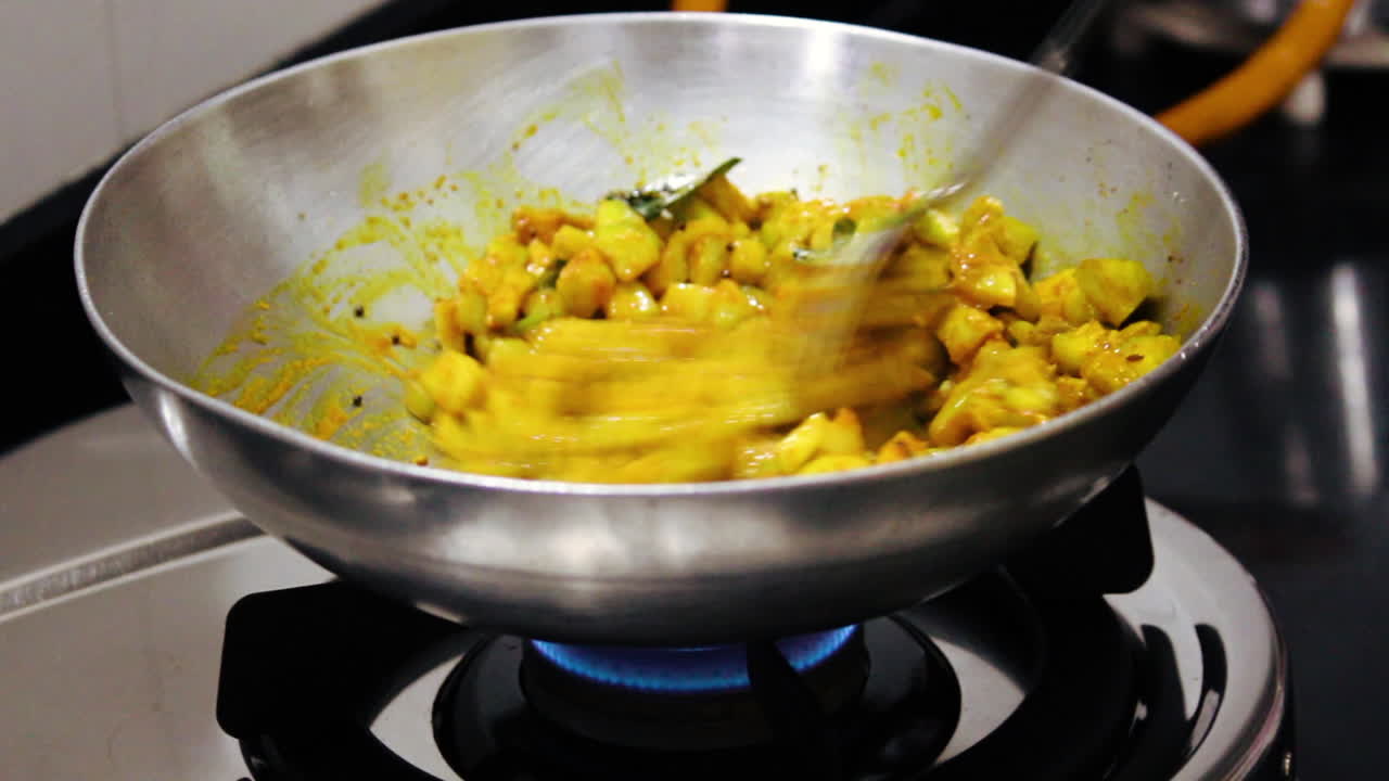 Close-up of Indian curry cooking in steel pan on gas stove. Vegetables and spices are stir-fried with ladle. Perfect for food, recipe and kitchen stock footage