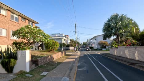 a suburban street scene with passing cars and pedestrians.