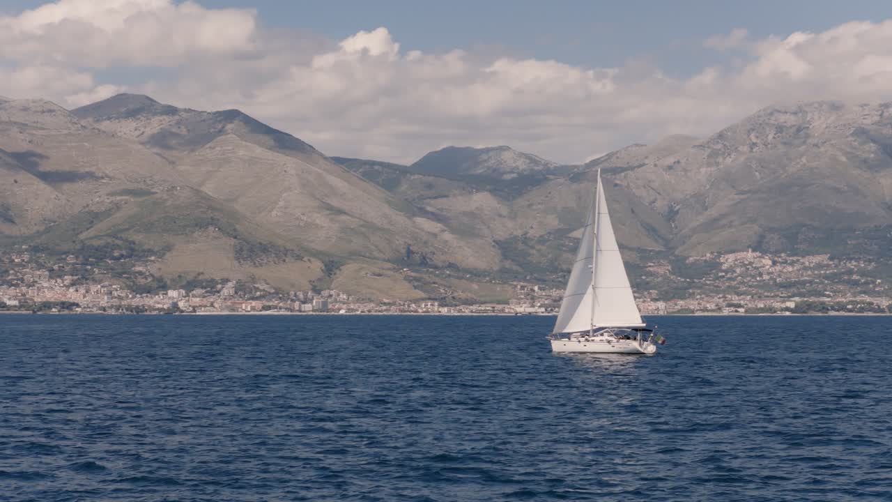 Una serena barca a vela scivola sulle acque blu con uno sfondo montuoso a Gaeta, Italia
