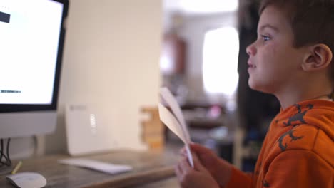 niño caucásico sentado frente a la computadora, haciendo su escuela primaria en línea
