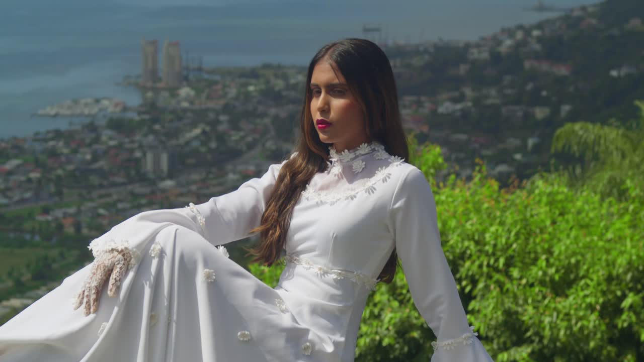 A young woman wearing a retro wedding gown stands atop an old fort.
