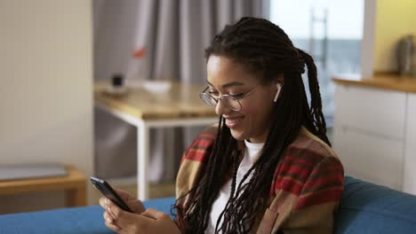 mujer joven usando un teléfono inteligente en casa en un sofá, vista lateral