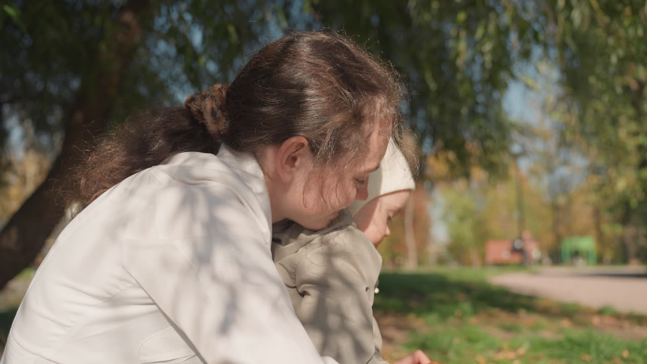 Momento tranquilo com mãe e bebê ao ar livre. Cena serena de uma mãe cuidando de seu filho sob a luz do sol. Cena familiar calma destacando o amor materno durante uma tarde pacífica de outono.