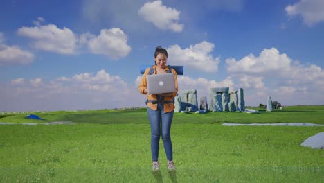 full body of asian female hiker with mountaineering backpack using a laptop while traveling in stonehenge