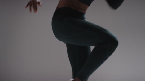 close up low angle shot of female athlete wearing tracksuit training in gym fitness class running on the spot against plain background 2