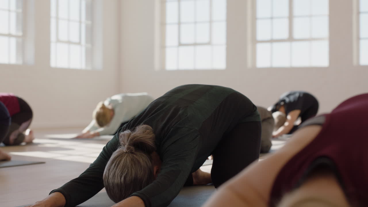 clase de yoga de mujeres maduras sanas que practican pose infantil disfrutando del ejercicio físico matutino en el estudio