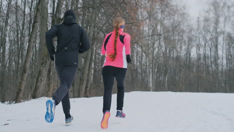 joven pareja familiar, hombre y mujer, corriendo por la mañana en el bosque de invierno. una mujer con una chaqueta holgada y un hombre con una chaqueta negra corre por un parque de invierno. estilo de vida saludable familia feliz