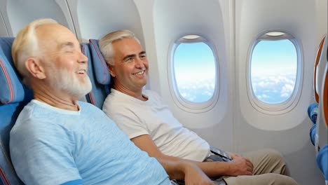 two men are sitting in an airplane, one of them smiling