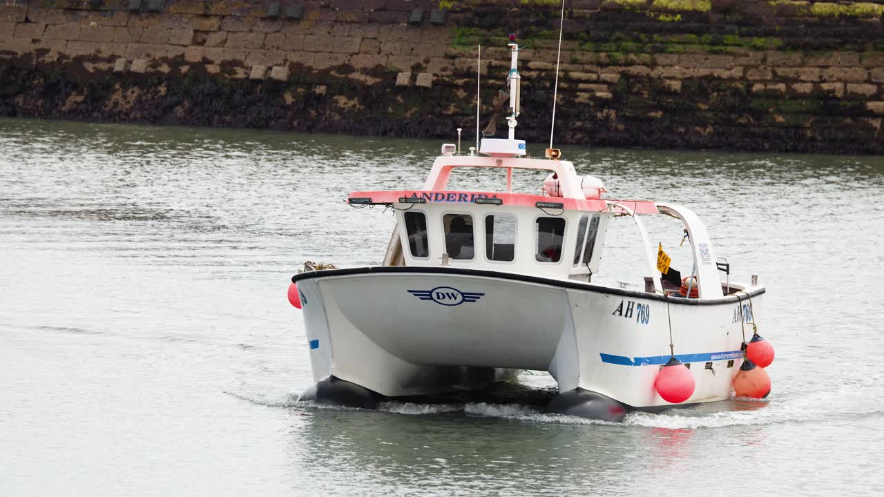 Small fishing boat moves steadily toward harbor wall in overcast daylight, captured with static camera