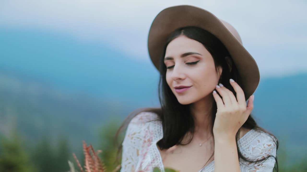 Portrait of brunette girl in nature. Beautiful young woman in hat and sexy dress posing at camera on the blurred nature background.
