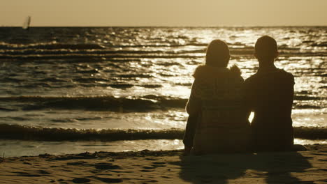 A-Loving-Couple-Sitting-Together-On-The-Sand-Admiring-The-Sea-And-The-Sunset-Sea-Swimming-Windsurfer