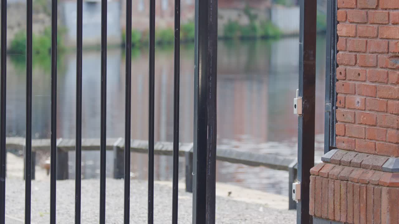 Black metal electric gate closes slowly against brick wall, outdoor daylight, fixed camera, urban environment