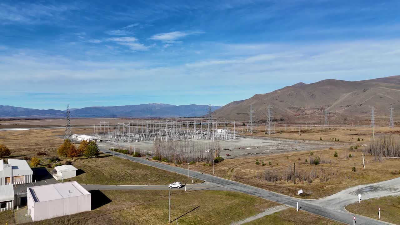 Aerial footage captures Lake Tekapo's power substation amidst autumn landscape, highlighting high voltage infrastructure under clear blue skies