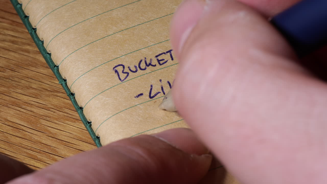 갈색 줄이 그어진 종이 저널에 목표를 살기 위해 자기 계발 버킷리스트 목표 설정을 작성하는 사람