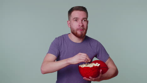 Bearded-young-man-basketball-fan-eating-popcorn-doing-winner-gesture,-celebrating-victory-win